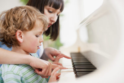 Piano teacher with a student at a white upright piano