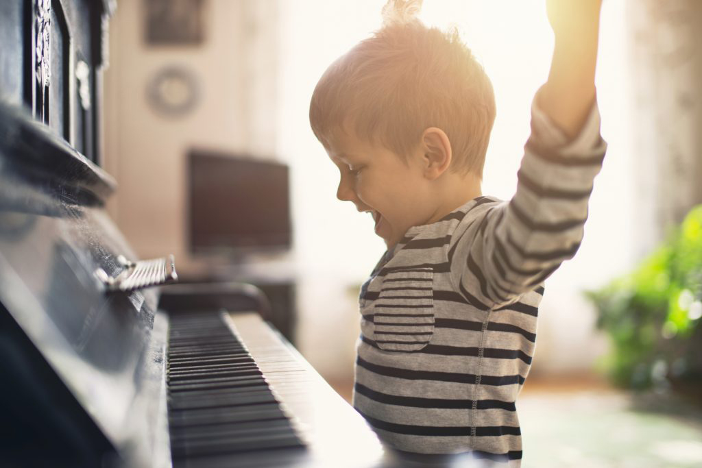 Child excitedly raising their hands above their head while playing an upright rental piano