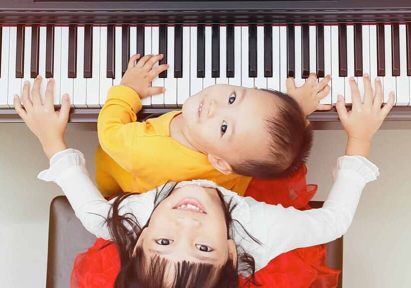 Two children playing a rental piano looking up at the camera