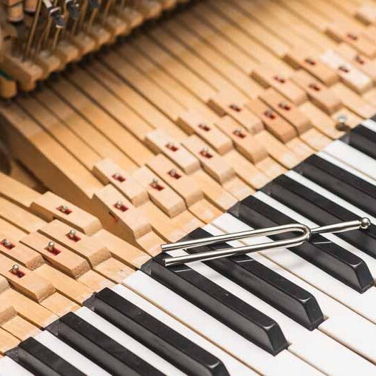 Piano technician tuning an upright piano, showing the professional service aspect of piano ownership.