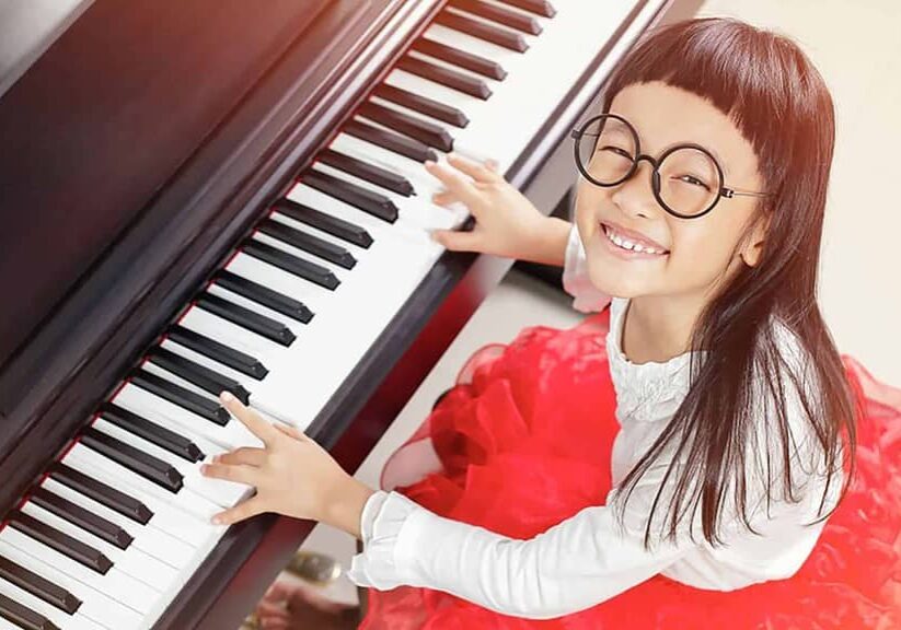 Girl with thick glasses and bangs smiling while playing piano